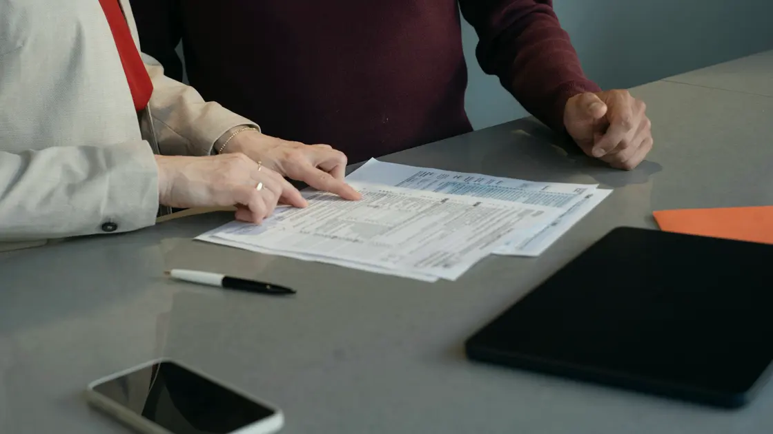 Two people at a desk going through a printed form, a phone and a tablet beside them